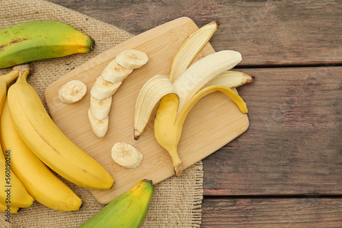 Whole and cut bananas on wooden table, flat lay. Space for text