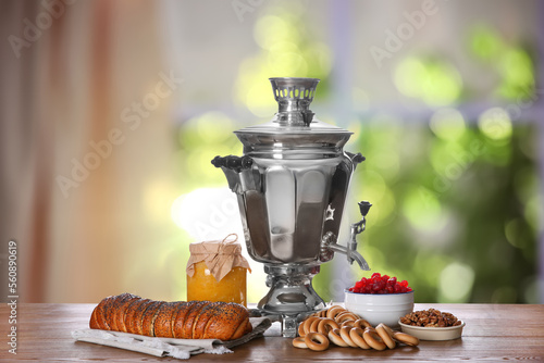 Traditional Russian samovar and treats on wooden table against window in room