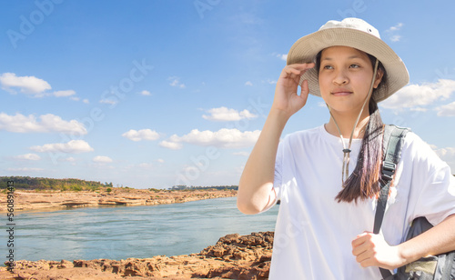 Portrait of a 14 year old Asian girl in a hat against a daytime river view.