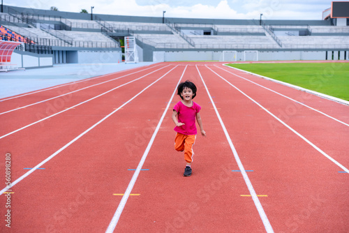 A girl in a pink sportswear and sneakers runs on the running track at the stadium outdoors. © kittipong