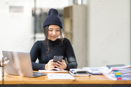 Cheerful business Asian woman freelancer using phone share good news about project working in office workplace, business finance concept.