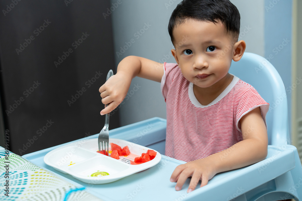 Happy toddler boy eating watermelon his high chair in dining room Happy toddler boy eating watermelon his high chair in dining room