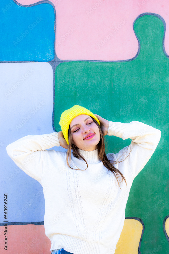 Happy playful young woman keeps hands on hat dressed in casual white jumper expresses emotions Happy playful young woman keeps hands on hat dressed in casual white jumper expresses emotions