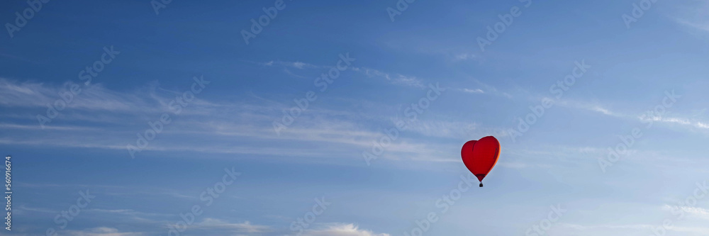 Fototapeta premium A colorful balloon in the shape of a heart, flying at sunset across the blue sky. Happy Valentine's Day Concept. Banner, space for text.