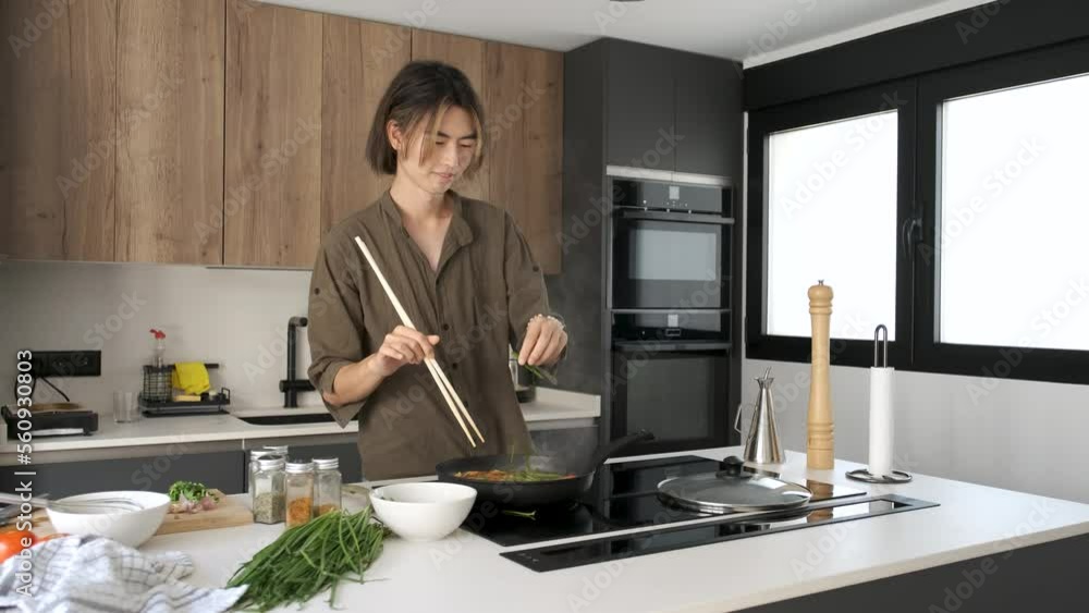 Asian young man adding chive to prepare chinese or taiwanese tomato scrambled eggs at kitchen. Asian young man adding chive to prepare chinese or taiwanese tomato scrambled eggs at kitchen.