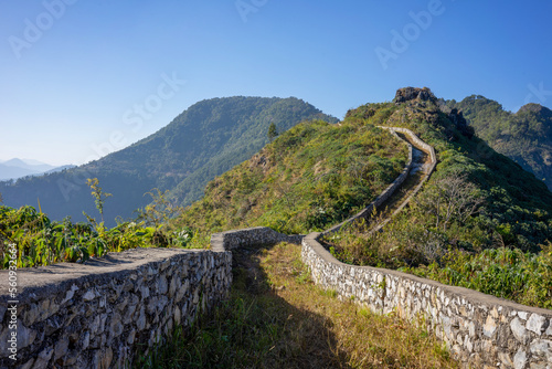 Curving path with dry stone wall leads over the mountains and hills at Bandipur Nepal on a sunny day with blue sky. The trail is reminiscent of the Great Wall of China. photo