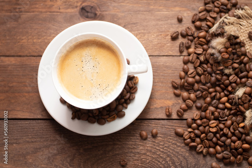 Cup of coffee on wooden table with roasted coffee beans on wooden background.