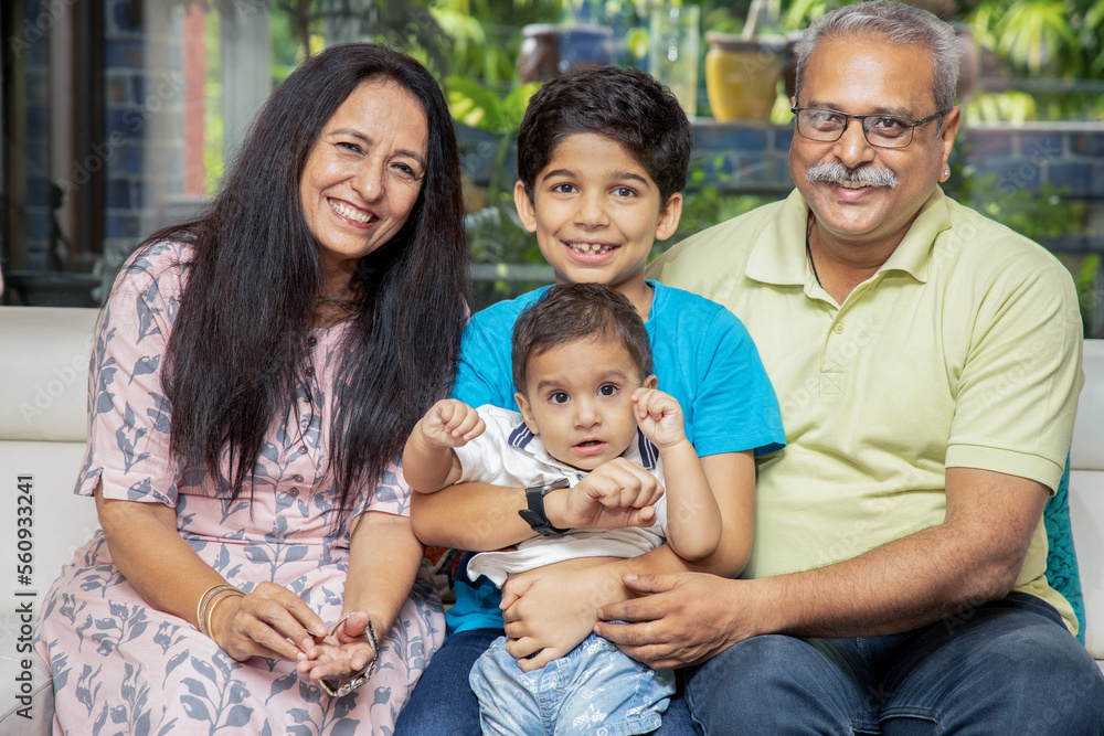 Portrait of Happy indian grand parents sitting with their grand children at home. Asian senior and young couple with kids looking at camera. Portrait of Happy indian grand parents sitting with their grand children at home. Asian senior and young couple with kids looking at camera.