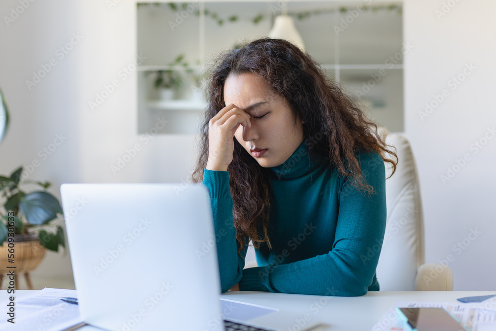 Exhausted Asian businesswoman having a headache in office. Creative woman working at office desk feeling tired. Stressed casual business woman feeling head pain while overworking on laptop computer. Exhausted Asian businesswoman having a headache in office. Creative woman working at office desk feeling tired. Stressed casual business woman feeling head pain while overworking on laptop computer.