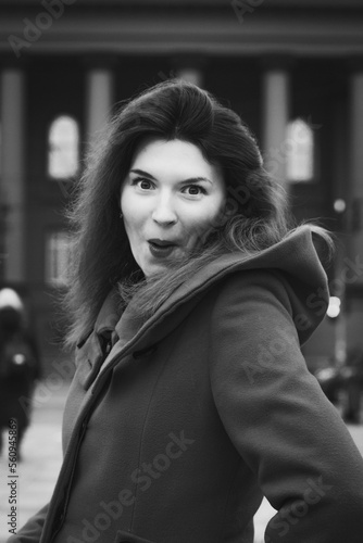 Close up amazed woman in stylish coat on street monochrome portrait picture. Closeup front view photography with building on background. High quality photo for ads, travel blog, magazine, article