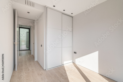 Empty clean bright bedroom with light wooden parquet and white wardrobe with sliding doors. A wardrobe is a useful and functional piece of furniture that saves space perfectly.