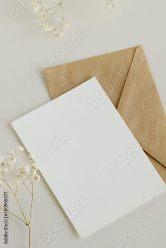 Greeting card mockup, envelope and dried gypsophila flowers twigs on beige background top view flatlay. Card mockup with copy space.