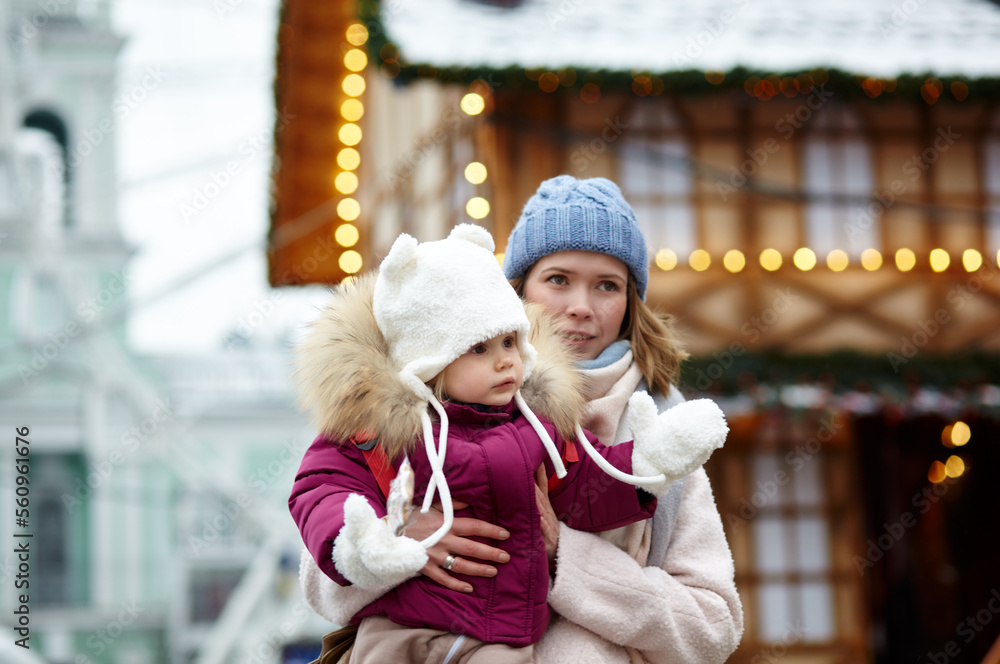 Obraz premium Mother and daughter are walking around the city on Christmas and New Year holidays. Parent and little child having fun outdoors