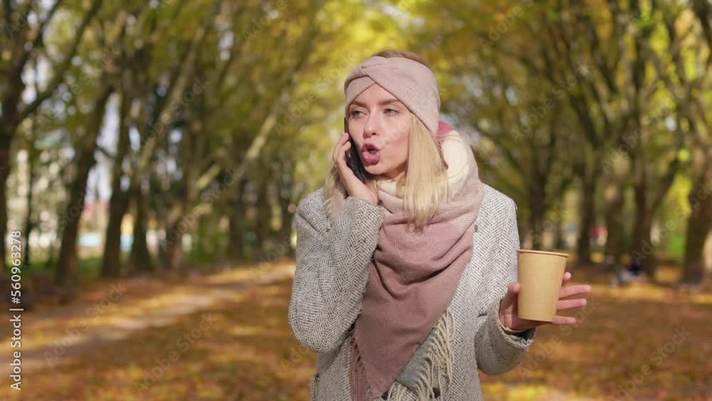 Front view of irritated, young lady standing in park, talking on smartphone. Beautiful female wearing stylish clothes, holding paper cup, busy. Concept of modern lifestyle. Front view of irritated, young lady standing in park, talking on smartphone. Beautiful female wearing stylish clothes, holding paper cup, busy. Concept of modern lifestyle.
