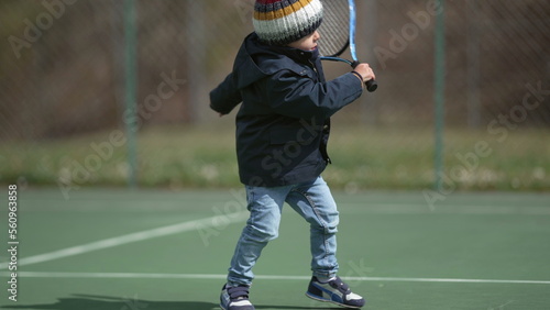 Child hitting ball with tennis racket wearing winter clothes during winter season. Kid playing sport © Marco