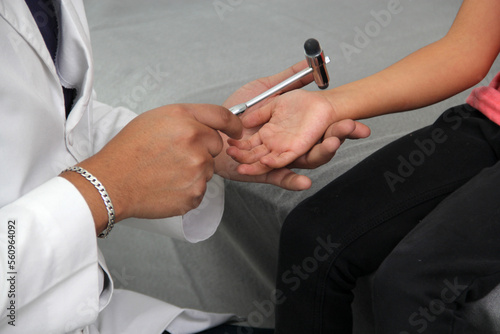 Latino doctor medic and girl patient in medical office checks her reflexes on hammer in her checkup to find disease diagnosis 