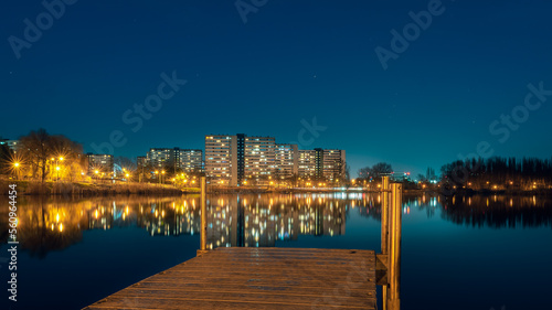 Night view on Tysiaclecie estate in Katowice, Silesia, Poland. Lightened residential buildings with surrounding trees at dusk seen through the lake. Little, wooden jetty in the foreground. photo