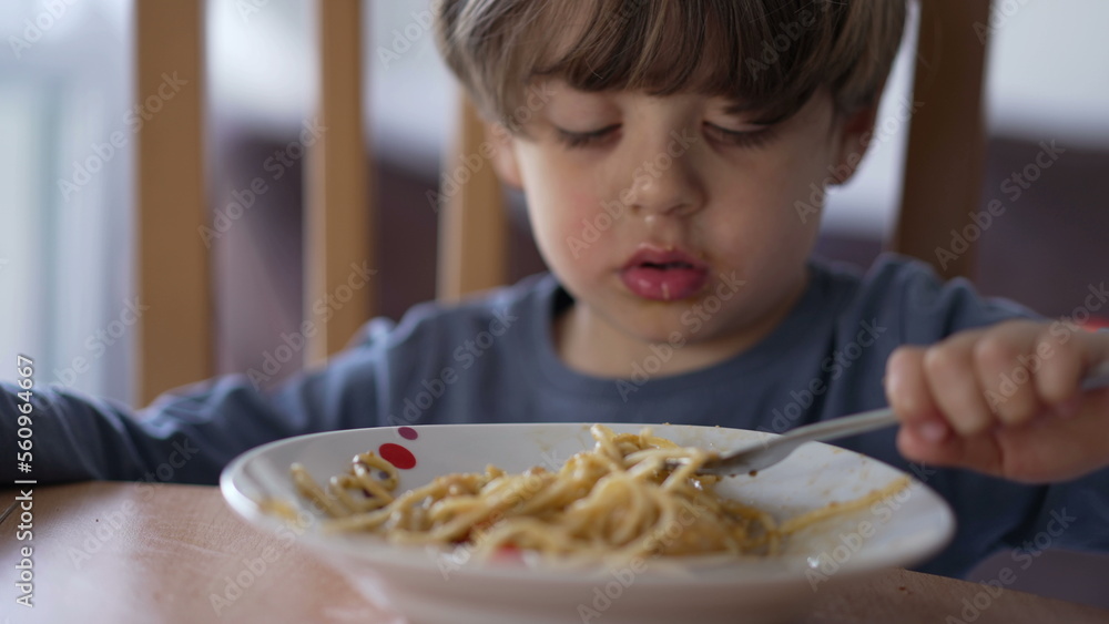 One little boy eating pasta with fork. Child eats lunch meal carb food. Kid nutrition concept One little boy eating pasta with fork. Child eats lunch meal carb food. Kid nutrition concept