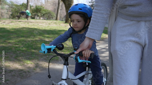 Little boy learning to ride bicycle with mother support. Mom helping child to ride bike outdoors
