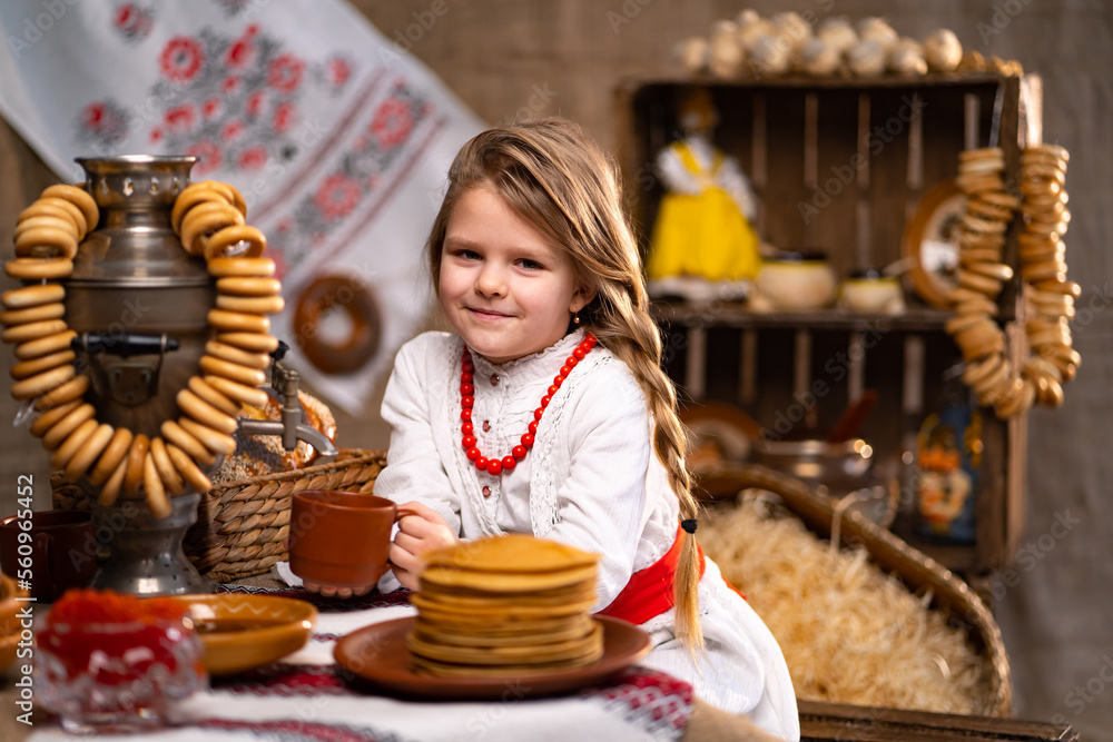 Little caucasian girl in national costume pouring tea from samovar while celebrating Maslenitsa. 