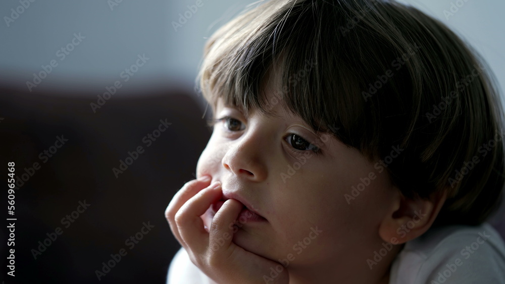 One small boy closeup face with hand in chin watching screen off camera. Focused child hypnotized by TV media content One small boy closeup face with hand in chin watching screen off camera. Focused child hypnotized by TV media content