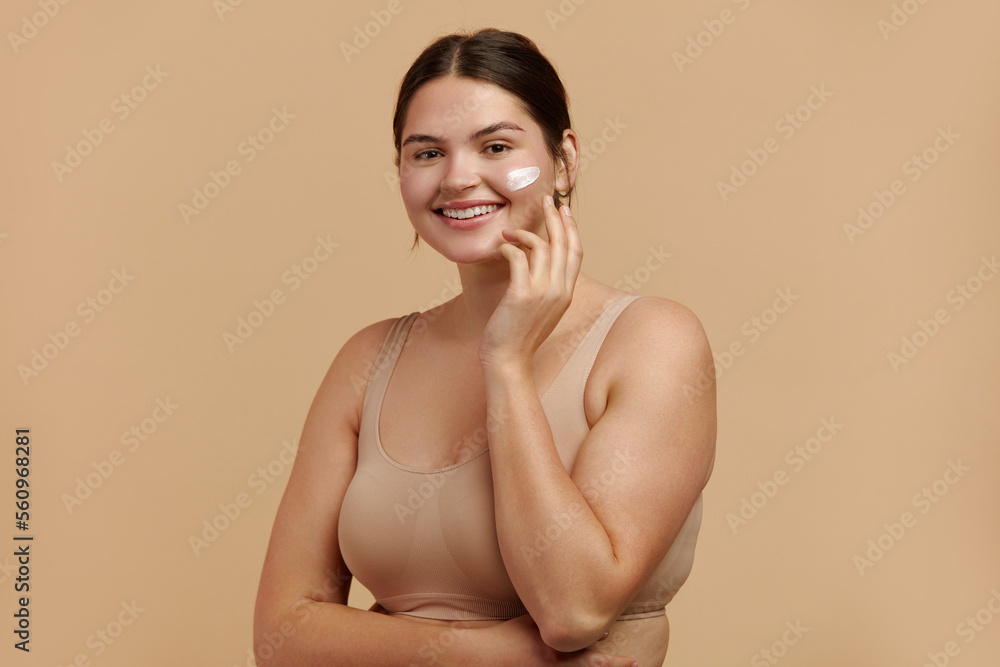 Obraz premium Positive Woman Applying Face Cream. Closeup Of Female Model With Fresh Skin Applying Cosmetic Product Under Eyes. Skincare Concept. High Resolution 