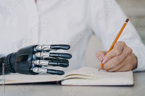 Cyber arm and healthy limb on the notebook. Woman with bionic prosthesis is studying remotely.