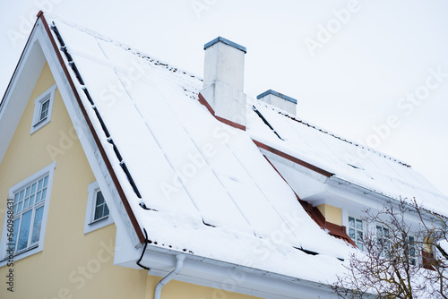 Close-up of snow covered solar panels installed on historic building gable roof with chimney. Private home using solar energy during winter with low efficiency.