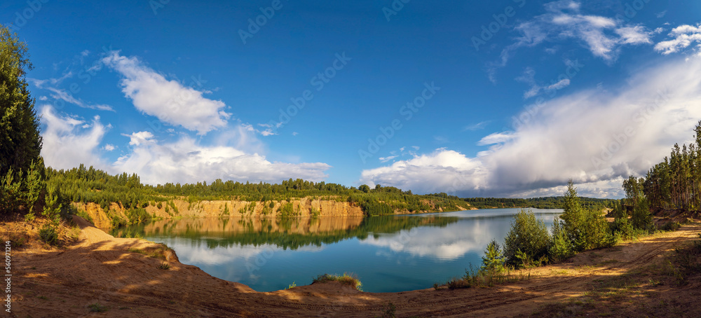 A high cliff with a path on the shore of a lake with snow-white clouds in the sky.