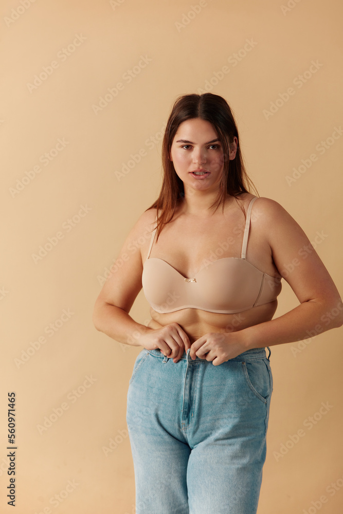 Plus Size Woman in Jeans. Sexy Overweight Woman Fastening Jeans And Looking At Camera. Body Positive People Concept Plus Size Woman in Jeans. Sexy Overweight Woman Fastening Jeans And Looking At Camera. Body Positive People Concept