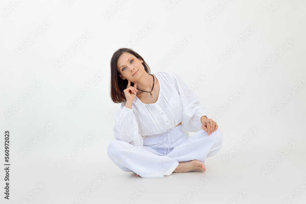 Portrait of young woman with short dark hair wearing white loose blouse, trousers, sitting on floor with crossed legs. Portrait of young woman with short dark hair wearing white loose blouse, trousers, sitting on floor with crossed legs.