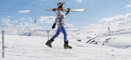 Young female with carrying skis and walking on a snowy hill photo