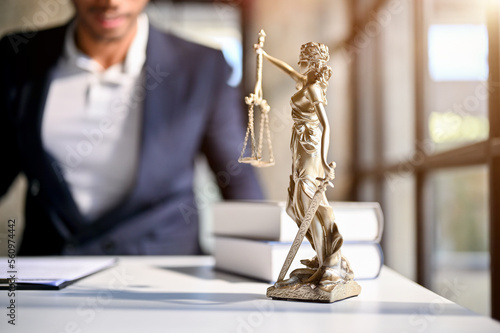 The Statue of Justice on a table over blurred background of professional male lawyer or attorney.
