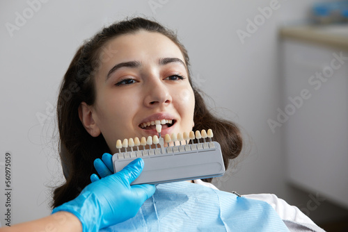 Dentist choosing color tone of tooth enamel for patient. Dentist applying sample from tooth enamel scale