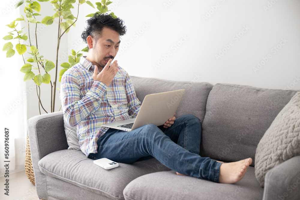 Fototapeta premium 部屋でパソコンの画面をみてびっくりするアジア系の男性 右にコピースペースあり