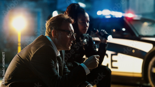 Portrait of Two Police Detectives Working on a Case at Night by Visiting a Crime Scene in a Back Alley. Focus on a Professional Criminologist Being Consulted as an Expert in Forensics and Murder Cases