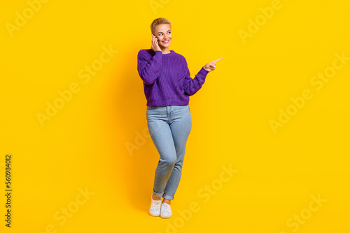Full length photo of attractive positive person look direct finger empty space speak telephone isolated on yellow color background