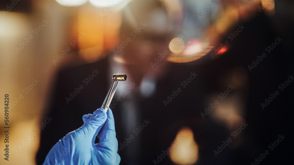Extreme Close Up with Blurry Background: Hand with Medical Glove Using Tweezers to Hold a Bullet Shell. Forensics Specialist Finding Cartridge on Crime Scene and Showing it to Detective as Evidence - obrazy, fototapety, plakaty 