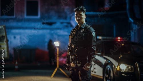 Wide Portrait Shot of a Young Asian Police Officer Holding a Flashlight and Looking Firmly at Camera in Siren Neon Lights. Policeman Reporting for Duty on a Crime Scene, Keeping Law and Order