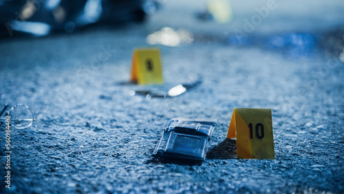 Low Angle Shot of Evidence Scattered at Crime Scene After Unfortunate Case of Mugging Gone Wrong. Numbered Markers are Next to Multiple Items Belonging to the Victim. Murder Weapon is on Site