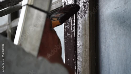 Close-up of a worker painting old wooden window frames while on a ladder