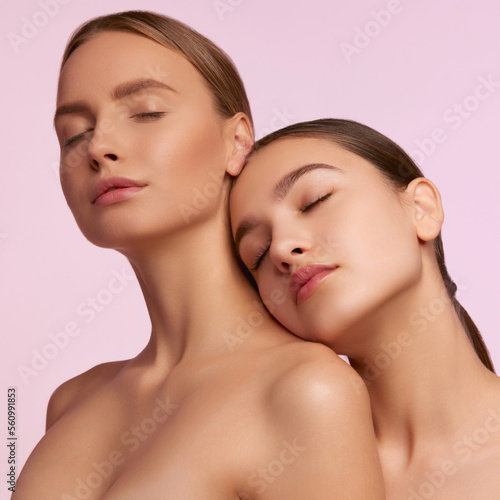 Tender self-care. Portrait of two young, beautiful girls with well-kept skin isolated over pink studio background. Concept of skincare, cosmetology, natural beauty