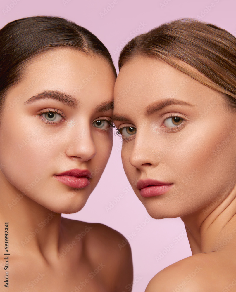 Perfect nude makeup. Portrait of two young, beautiful girls with well-kept skin isolated over pink studio background. Concept of skincare, cosmetology, natural beauty Perfect nude makeup. Portrait of two young, beautiful girls with well-kept skin isolated over pink studio background. Concept of skincare, cosmetology, natural beauty