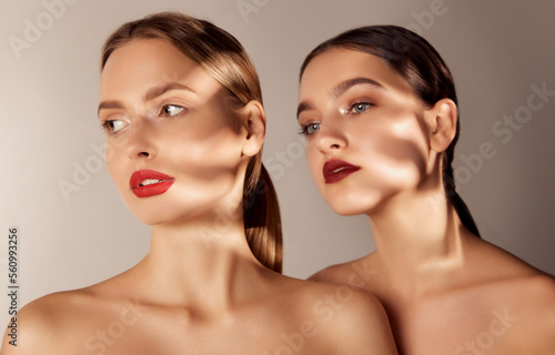 Portrait of two young  beautiful blonde and brunette girls with red lips makeup isolated over grey studio background. Shadows. Concept of skincare  cosmetology  natural beauty