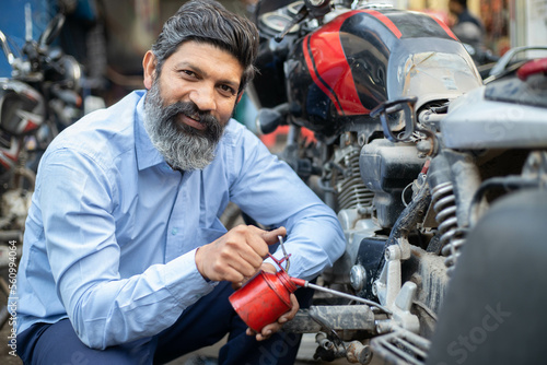Professional Indian mechanic repairs motorcycle give oil to it. Asian man repairing motorbike in repair shop.