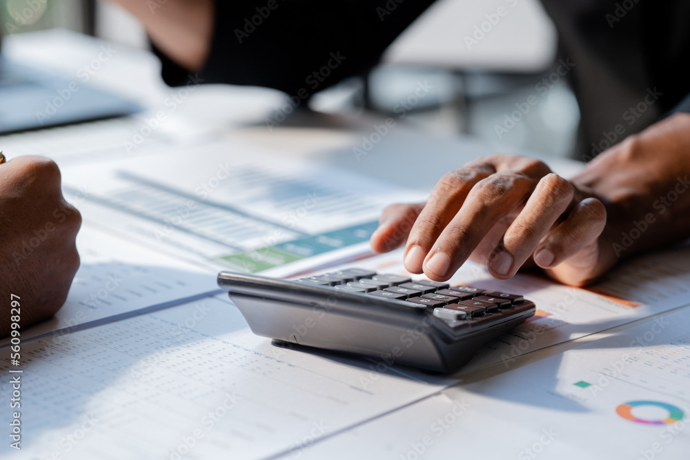 Fototapeta premium Businessman using a calculator to calculate numbers on a company's financial documents, he is analyzing historical financial data to plan how to grow the company. Financial concept.