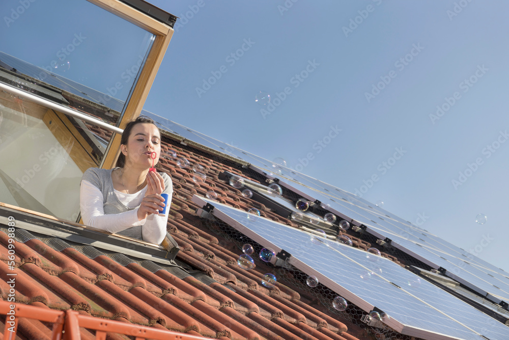 Woman blowing bubbles out of roof window with solar panels Woman blowing bubbles out of roof window with solar panels