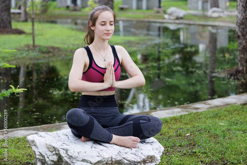young happy and healthy woman meditation on the rock near pond at public park background.  woman practices yoga and meditates with calm and peachful. outdoor excercise concept. photo