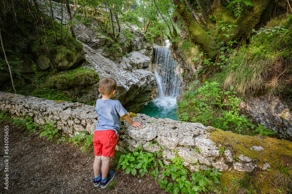 Cute blonder boy admires small beautiful mountain waterfall