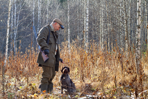 a hunter and his hunting dog are in a thicket of withered grass near a birch grove